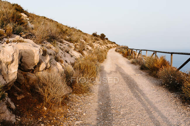Unerkennbare Menschen im Schatten eines schmalen Feldweges mit Holzzaun, der an nebligen Tagen in Küstennähe entlang des Gebirges führt — Stockfoto