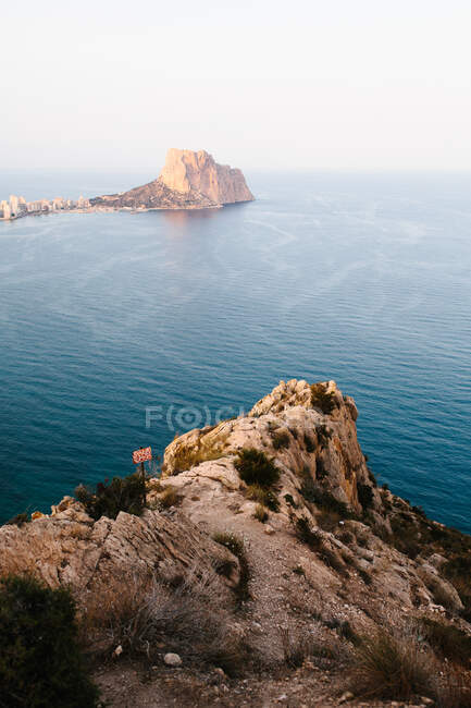 High angle view of calm sea rippling near rough rocky shore with stony cliff rising over water in distance — Stock Photo