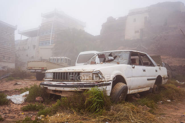 Vehicle with shattered windshield located on junkyard on misty day on street of grungy town — Stock Photo