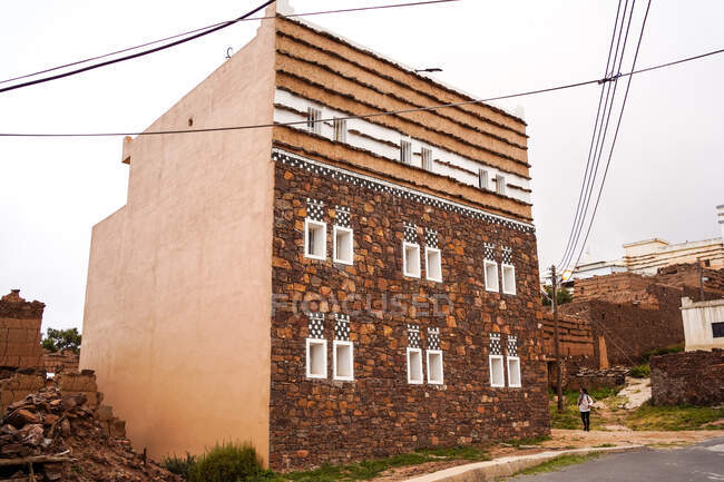 Extérieur du bâtiment résidentiel avec des ornements traditionnels sur la façade situé près d'une personne éloignée le jour gris sur la rue de la ville — Photo de stock