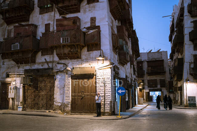 Bâtiments typiques en pierre résidentielle avec murs et balcons minables sur la vieille rue de la ville de Jeddah en Arabie Saoudite la nuit avec des gens qui marchent — Photo de stock