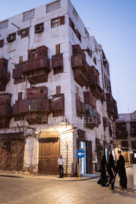 Typical residential stone buildings with shabby walls and balconies on old street of Jeddah city in Saudi Arabia at night time with walking people — Stock Photo