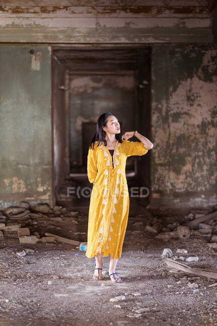 Corps complet jeune Asiatique femme en robe traditionnelle safran debout dans le couloir de la vieille maison en pierre abandonnée dans la ville de Jeddah en Arabie Saoudite — Photo de stock
