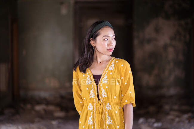 Young Asian female in traditional saffron dress standing in corridor of old abandoned stone house in Jeddah city in Saudi Arabia — Stock Photo