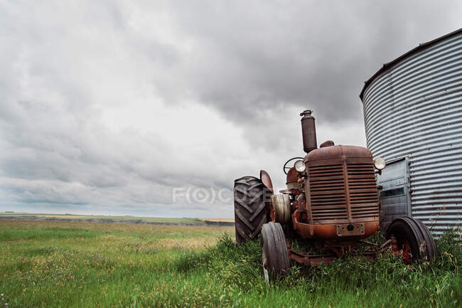 Bajo ángulo de máquina agrícola oxidada con enormes ruedas estacionadas en el césped verde cerca de granero en el campo - foto de stock