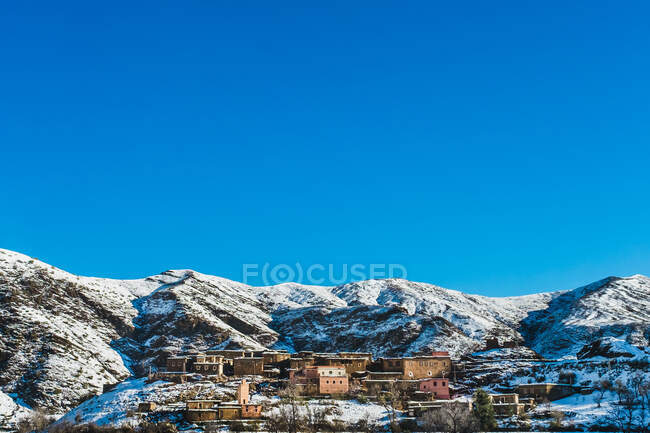 Casas residenciales en pendiente de montaña cubiertas de nieve y cielo azul - foto de stock
