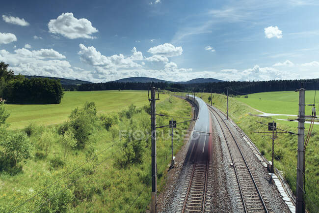 Вид на безпілотник величний краєвид поїзду, що їде залізницею в оточенні зелених полів і гір у сонячний день — стокове фото