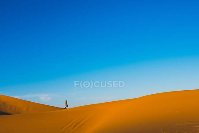 Vista lateral da incrível paisagem do deserto com turista solitário passeando ao longo da duna de areia durante o pôr do sol em Marrocos — Fotografia de Stock