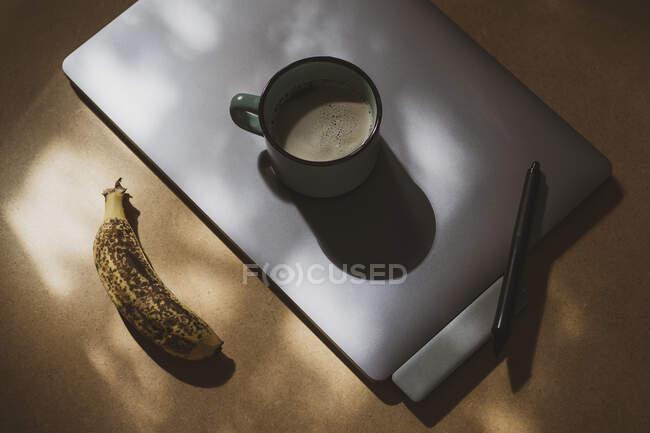 Caneca de café em comprimido gráfico com caneta e banana madura à luz do sol — Fotografia de Stock