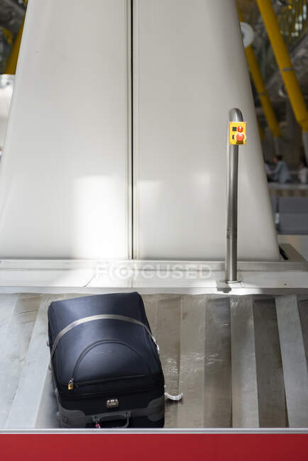 Metal baggage conveyor belt with suitcase near red emergency button at empty airport terminal — Stock Photo