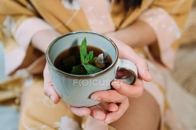 Donna rilassata senza volto in abiti da casa in possesso di tazza di tè gustoso mentre godendo il tempo libero a casa — Foto stock
