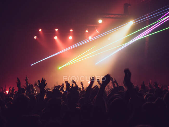 Siluetas retrovisoras de personas contra el escenario iluminado con luces durante la interpretación musical - foto de stock