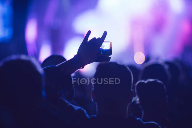 Visão traseira silhueta de pessoa irreconhecível fazendo vídeo com smartphone enquanto assiste show moderno contra palco de néon iluminado — Fotografia de Stock