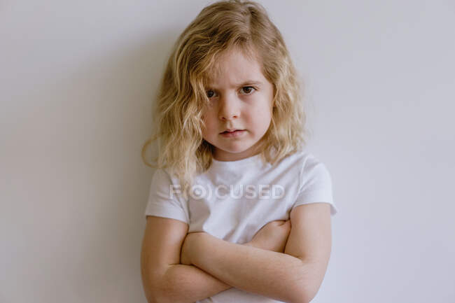 Разочарованный маленький ребенок в повседневной футболке смотрит на камеру на белом фоне в студии — стоковое фото