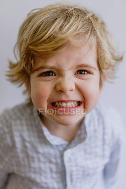 Entzückendes kleines Kind in lässigem Hemd, lächelnd und grimmig, während es in die Kamera auf weißem Hintergrund des Studios blickt — Stockfoto