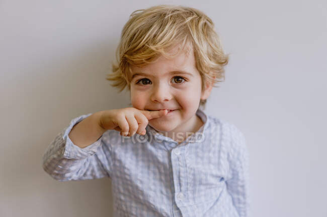 Adorable niño pequeño con camisa casual sonriendo y mirando a la cámara en el fondo blanco del estudio - foto de stock