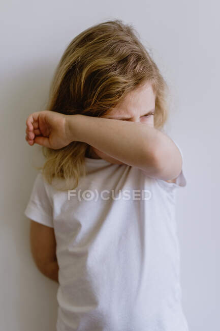 Freches Kind mit welligem Haar in lässiger Kleidung, das mit verschränkten Armen steht und weinend auf weißem Hintergrund wegschaut — Stockfoto