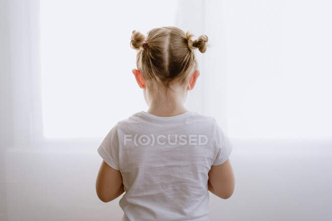 Vista trasera de niño deprimido irreconocible en traje casual de pie en apartamento luminoso - foto de stock