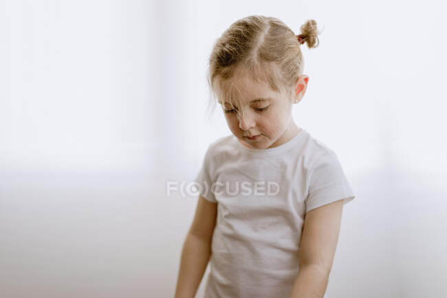 Enfant positif portant des vêtements décontractés debout sur un mur blanc dans un studio moderne — Photo de stock