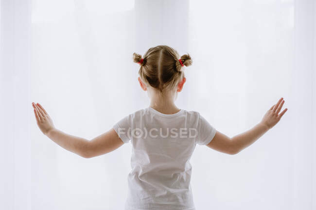 Обратный вид на неузнаваемого малыша в повседневной одежде, стоящего в яркой квартире и вытягивающего руки во время танцев — стоковое фото