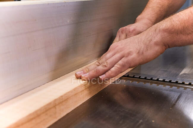 Trabajador de madera masculino en ropa casual enfocando y cortando madera usando una máquina eléctrica especial mientras trabaja en un taller moderno y ligero - foto de stock