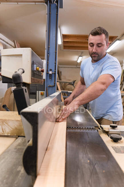 Male woodworker in casual clothes focusing and cutting lumber using special electric machine while working in light modern workshop — Stock Photo