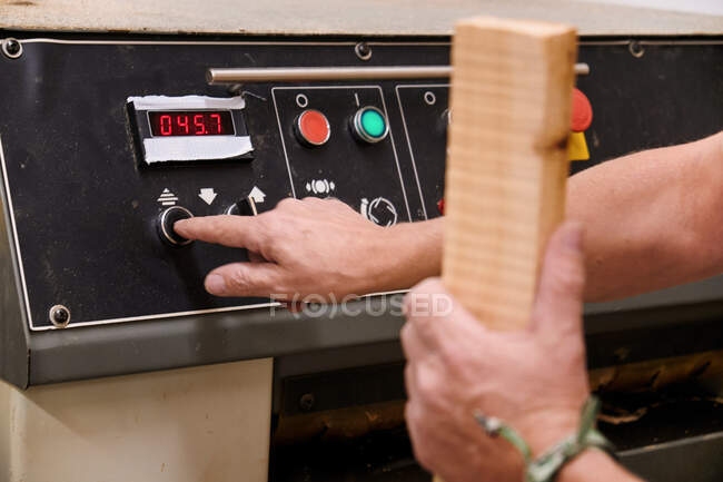 Low angle of unrecognizable woodworker setting up special planning electric machine before using while working with timber in light modern workroom — Stock Photo