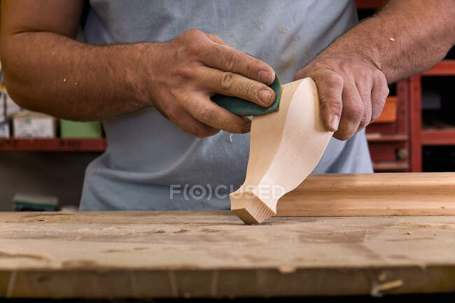 Niedriger Winkel des gesichtslosen Tischlers poliert Holzdetails mit Schleifpapier, während er in einem leichten modernen Arbeitsraum arbeitet — Stockfoto