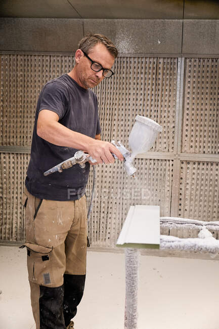 Konzentrierter Handwerker mit Airbrush zum Auftragen von Flammschutzmitteln auf Holzdetails, die den Brandschutz in der Tischlerei gewährleisten — Stockfoto
