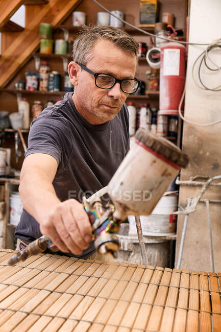 Artesanato aplicando verniz em madeira jalousie usando aerógrafo em oficina de carpintaria — Fotografia de Stock