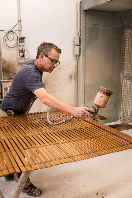 Artesanato aplicando verniz em madeira jalousie usando aerógrafo em oficina de carpintaria — Fotografia de Stock