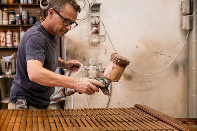 Крефтсмен застосовує лак до деревної джалузі за допомогою пензля у теслярській майстерні. — стокове фото