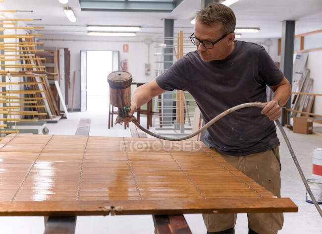 Craftsman applying varnish to wood jalousie using airbrush in carpentry workshop — Stock Photo
