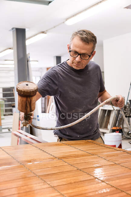 Ремесленник наносит лак на древесину жалюзи с помощью аэрографии в столярной мастерской — стоковое фото