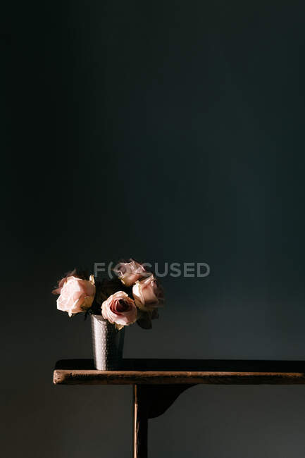 Blooming fresh pink roses in vintage vase placed on wooden table at black wall in modern apartment — Stock Photo