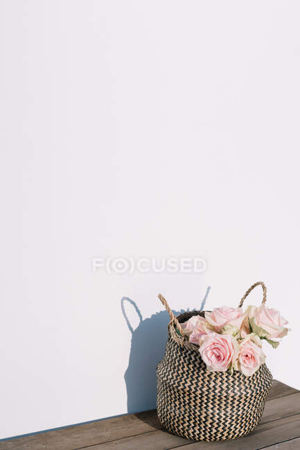 Bunch of fresh pink roses in wicker basket placed on wooden table near white wall in modern light apartment — Stock Photo