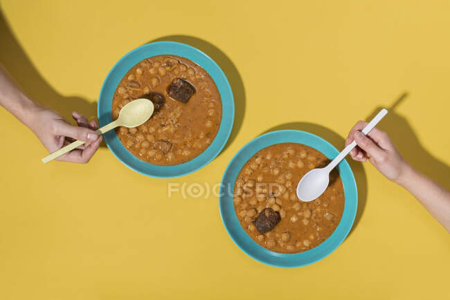 Vista superior de duas mãos com pratos Callos sobre fundo amarelo — Fotografia de Stock