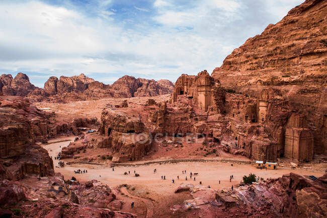Видовищний повітряний вид на літню визначну пам'ятку в скелястій пустелі з горами з відвідувачами, розташованими на тлі хмарного блакитного неба в сонячний день — стокове фото