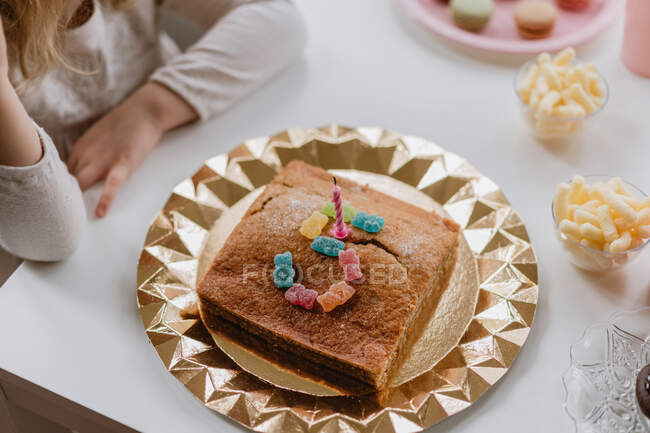 Сверху вид вкусного праздничного торта, украшенного свечами и желейными конфетками, помещенными в виде номера пять на столе в комнате — стоковое фото