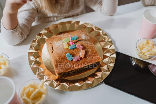 From above view of tasty birthday cake decorated with candle and jelly candies placed in shape of number five on table in room — Stock Photo