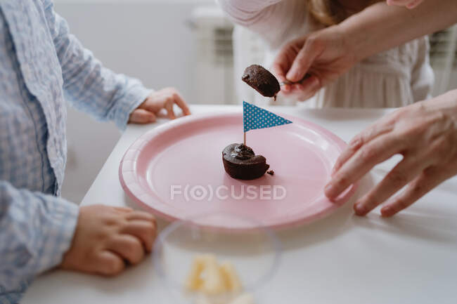 Mujer sin rostro compartiendo dulce postre de chocolate con bandera en plato rosa con los niños en casa - foto de stock