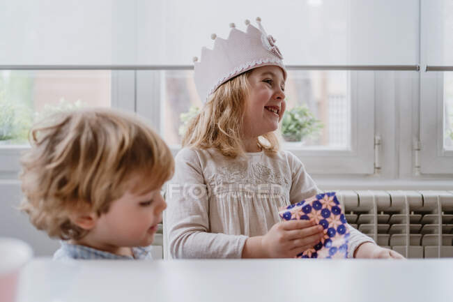 Aufgeregt charmantes Mädchen in handgemachter Krone Auspacken Geschenkbox während der Geburtstagsfeier zu Hause — Stockfoto