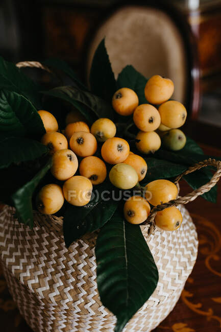Wicker basket with fresh loquat fruits and green leaves — Stock Photo