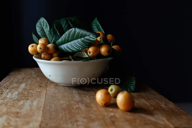 Bol en céramique blanche avec de savoureux fruits et feuilles de loquat — Photo de stock