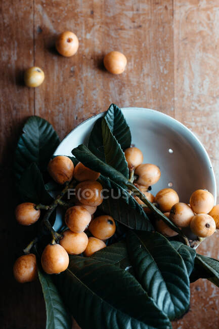 Ciotola in ceramica bianca con gustosi frutti loquat e foglie — Foto stock