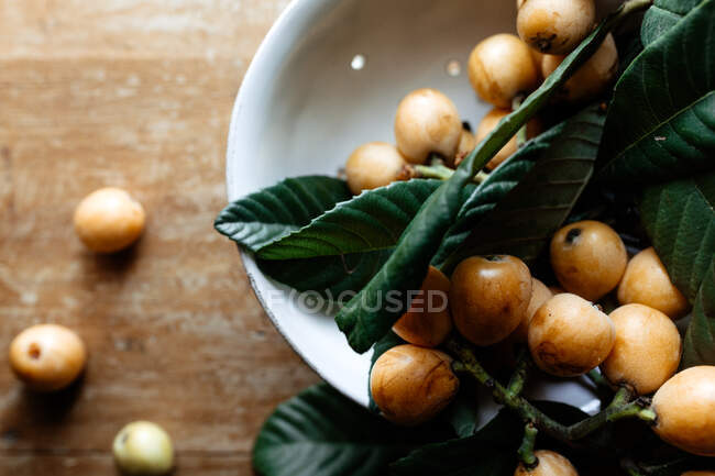 Ciotola in ceramica bianca con gustosi frutti loquat e foglie — Foto stock
