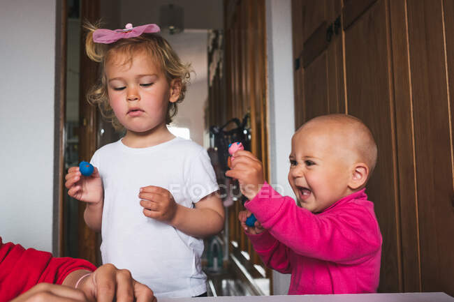Petits enfants joyeux et mignons en vêtements décontractés jouant avec la plasticine tout en passant du temps ensemble à la maison — Photo de stock
