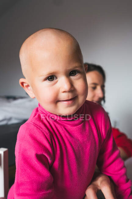 Lindo niño en camisa rosa casual de pie en el suelo en la sala de juegos de luz y mirando a la cámara mientras pasa tiempo en casa - foto de stock