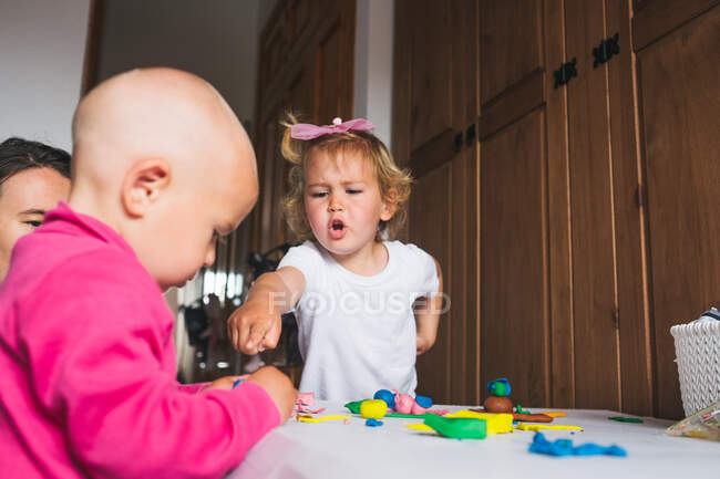 Carino allegri bambini in abiti casual giocare con la plastilina mentre trascorrono del tempo insieme a casa — Foto stock