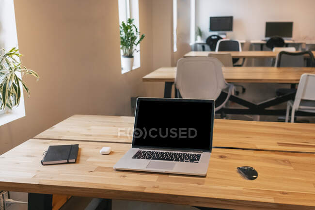 Netbook and mouse placed on wooden table with notebook and wireless earphones in creative workspace — Stock Photo